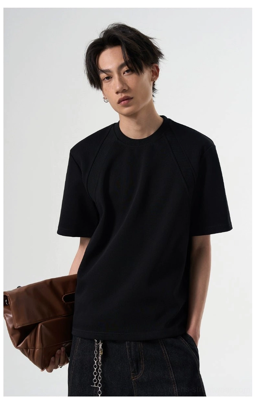 Black solid-color raglan sleeve streetwear T-shirt shown from the side with chain-detail pants and a brown leather clutch