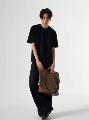 Black relaxed raglan short-sleeve T-shirt shown in a three-quarter front view with a structured crew neck and brown leather tote