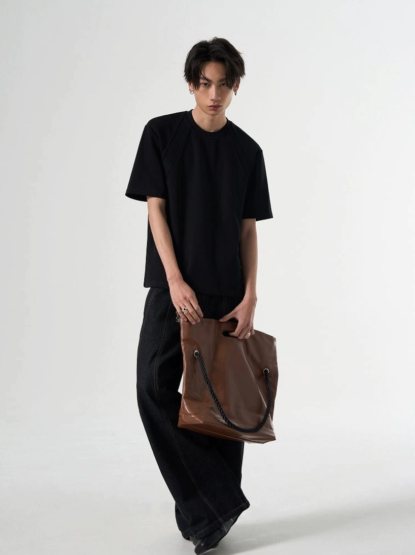 Black relaxed raglan short-sleeve T-shirt shown in a three-quarter front view with a structured crew neck and brown leather tote
