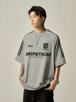 Oversized grey football-themed raglan graphic tee straight front portrait streetwear look with AWSPIKYHEAD branding and shield logos on chest