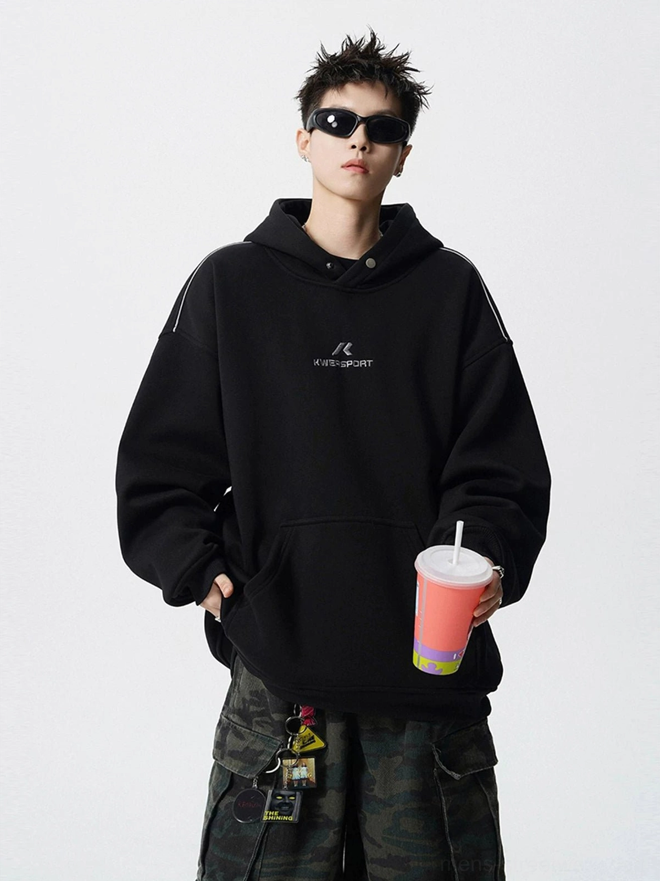 Black oversized sport hoodie with embroidered chest detail, dropped shoulders, kangaroo pocket, and relaxed Korean streetwear fit styled with camo cargo pants