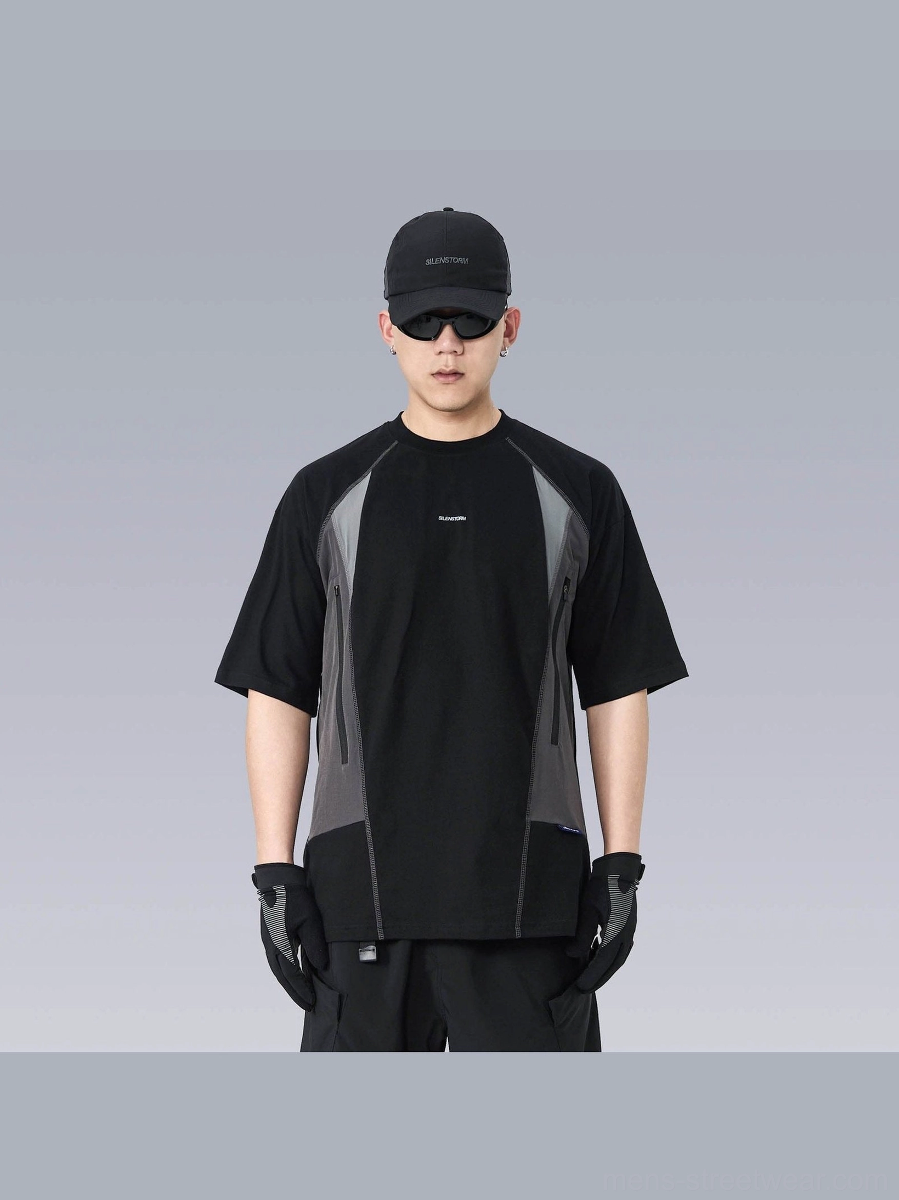 Front view of an oversized black and grey techwear panel T-shirt with relaxed fit, short sleeves, small chest graphic, black cargo pants, cap, and gloves