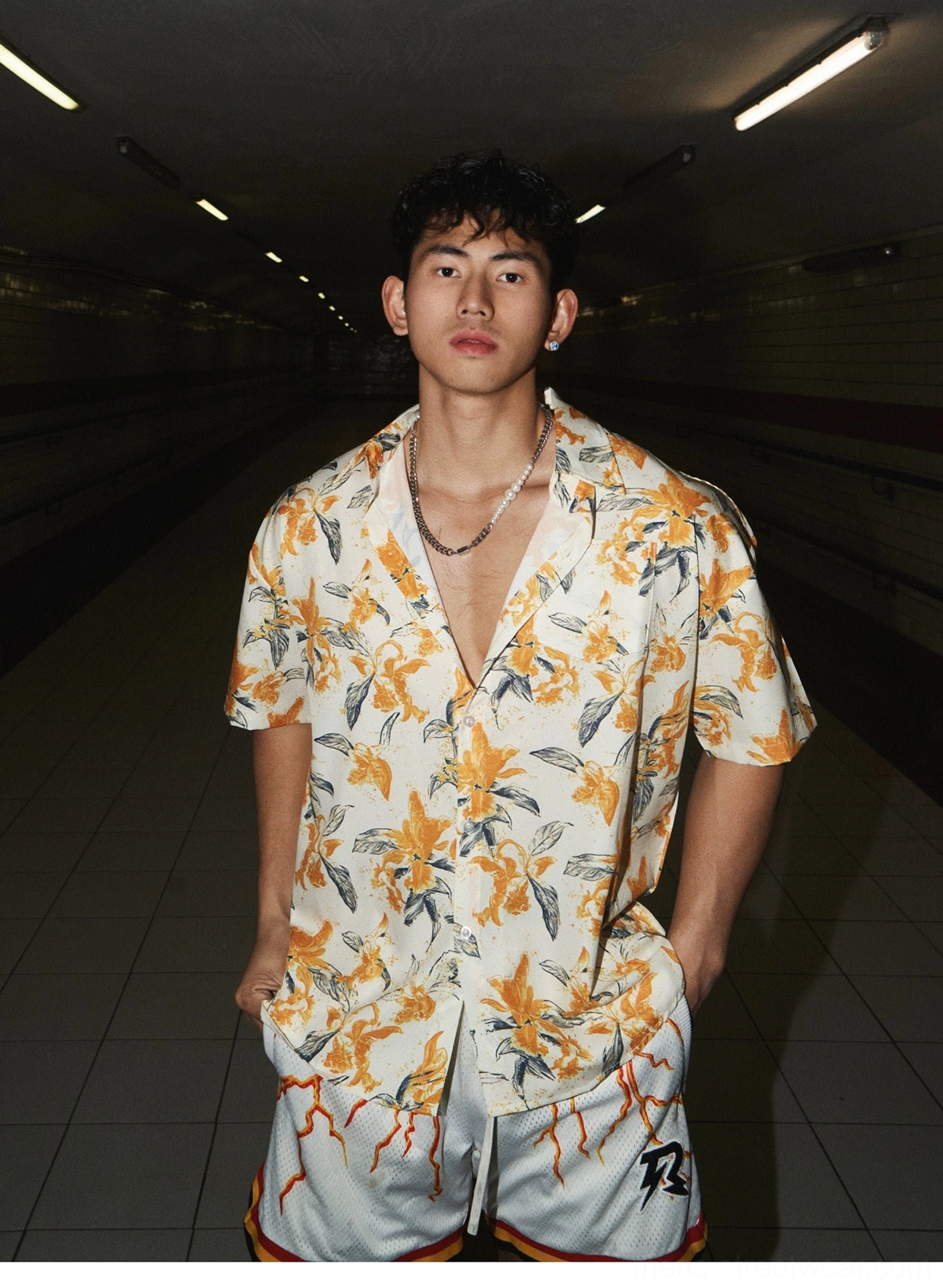 Front view of an oversized tropical floral camp shirt styled with flame print athletic shorts and a silver necklace