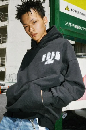 Black oversized graphic hoodie with white chest print, attached hood, kangaroo pocket, and relaxed Korean streetwear fit on an urban Japanese street