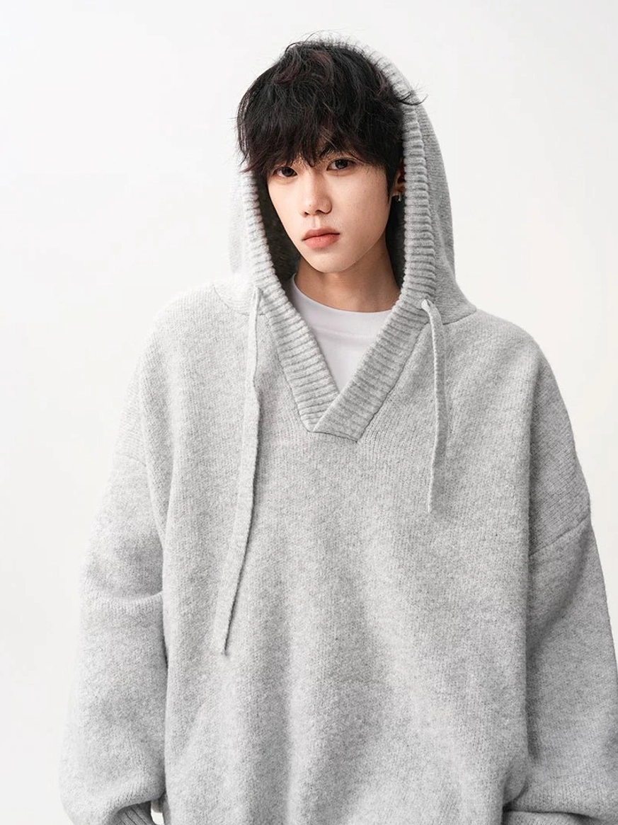 Light gray brown oversized V-neck knit hoodie worn with hood up showing ribbed neckline and drawstrings
