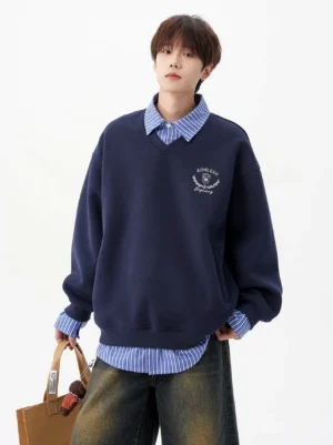 Navy blue oversized V-neck layered sweatshirt with embroidered collegiate crest, striped shirt layering, and relaxed Korean streetwear styling