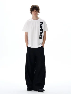 Model wearing an oversized white vertical script graphic T-shirt with raised lettering styled with wide-leg black streetwear pants