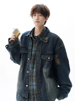 Blue oversized vintage distressed denim jacket with faded wash, sleeve patches, chest pockets, and layered plaid shirt streetwear styling