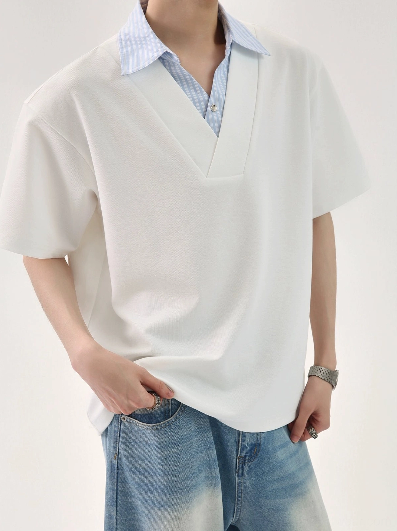 Front close-up of an oversized white faux layered streetwear T-shirt with blue striped shirt collar and V-neck placket styled with faded blue jeans