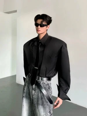 Black oversized wide-shoulder streetwear dress shirt with long sleeves styled with washed gray jeans in minimalist studio