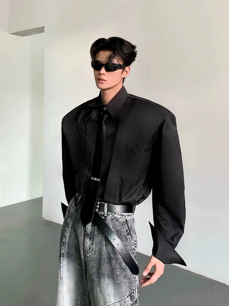 Black oversized wide-shoulder streetwear dress shirt with long sleeves styled with washed gray jeans in minimalist studio