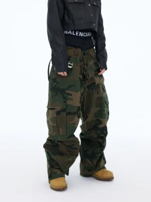 Front view of oversized woodland camouflage mega cargo pants with ultra-baggy stacked wide legs, large utility pockets, adjustable waist straps, and yellow work boots