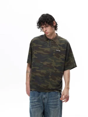 Front three quarter view of an oversized woodland camouflage polo shirt styled with wide leg blue jeans in a minimalist studio