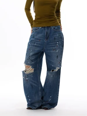 Paint splatter distressed ultra wide leg denim jeans in blue shown from a low three-quarter front view with frayed ripped knees
