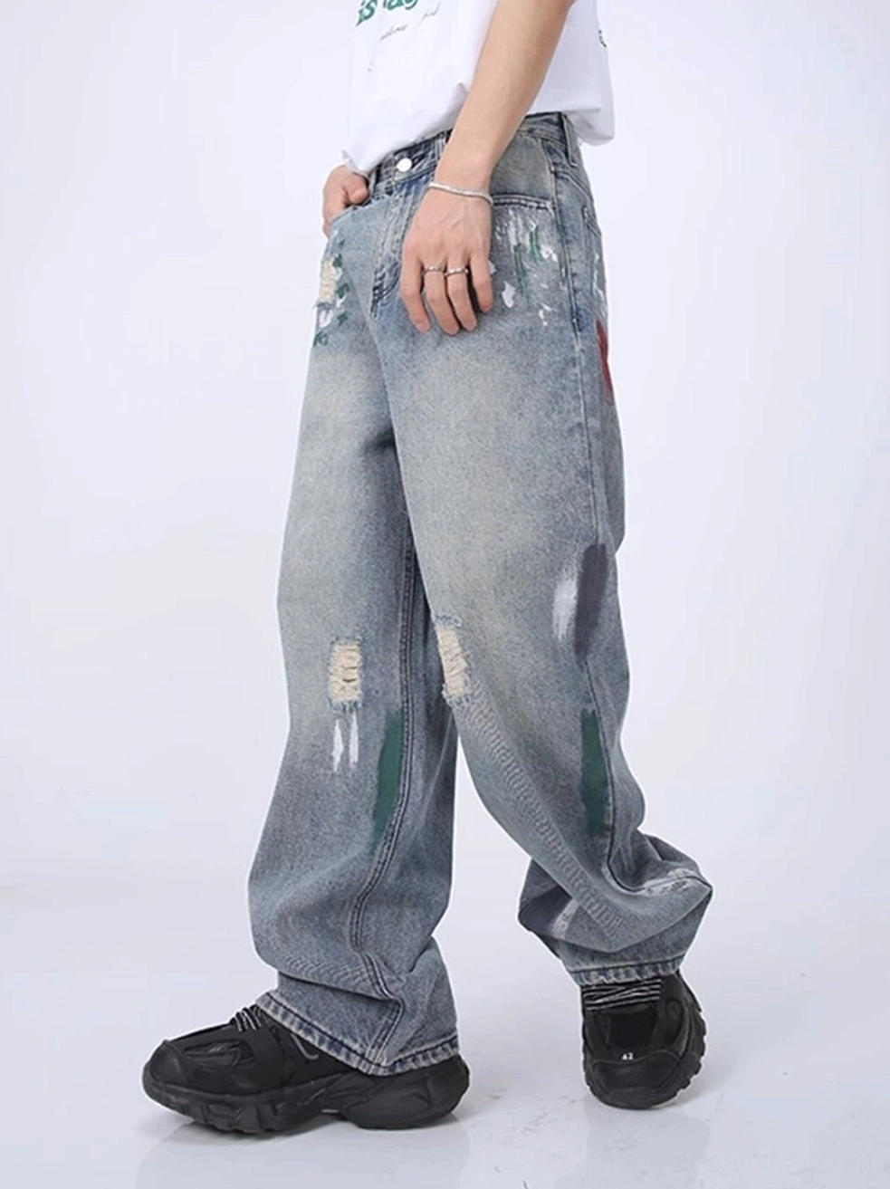 Left side view of light wash distressed wide leg jeans with colorful paint splatters, raw tears, and vintage denim texture