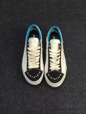 Pair of matching white pearl-studded skate sneakers viewed from above with black toe caps, blue accents, lace-up fronts, and embellished streetwear detailing