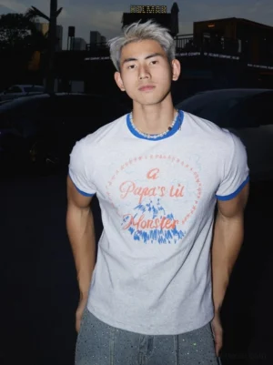 Front close-up of light grey Papa's Lil Monster graphic ringer tee with blue contrast collar and sleeve cuffs styled with a pearl beaded necklace