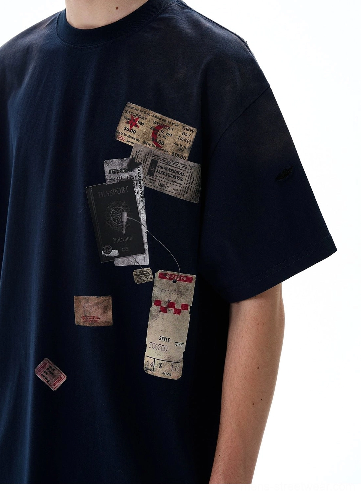 Close-up of vintage passport stamp, luggage tag, and travel ticket graphics on a washed oversized cotton T-shirt