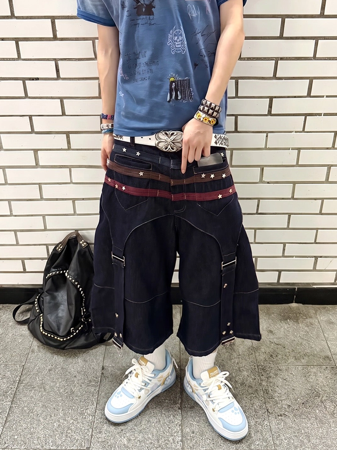 Unisex paw print streetwear sneakers styled with wide-leg cropped denim, blue graphic tee, layered belts, and black backpack