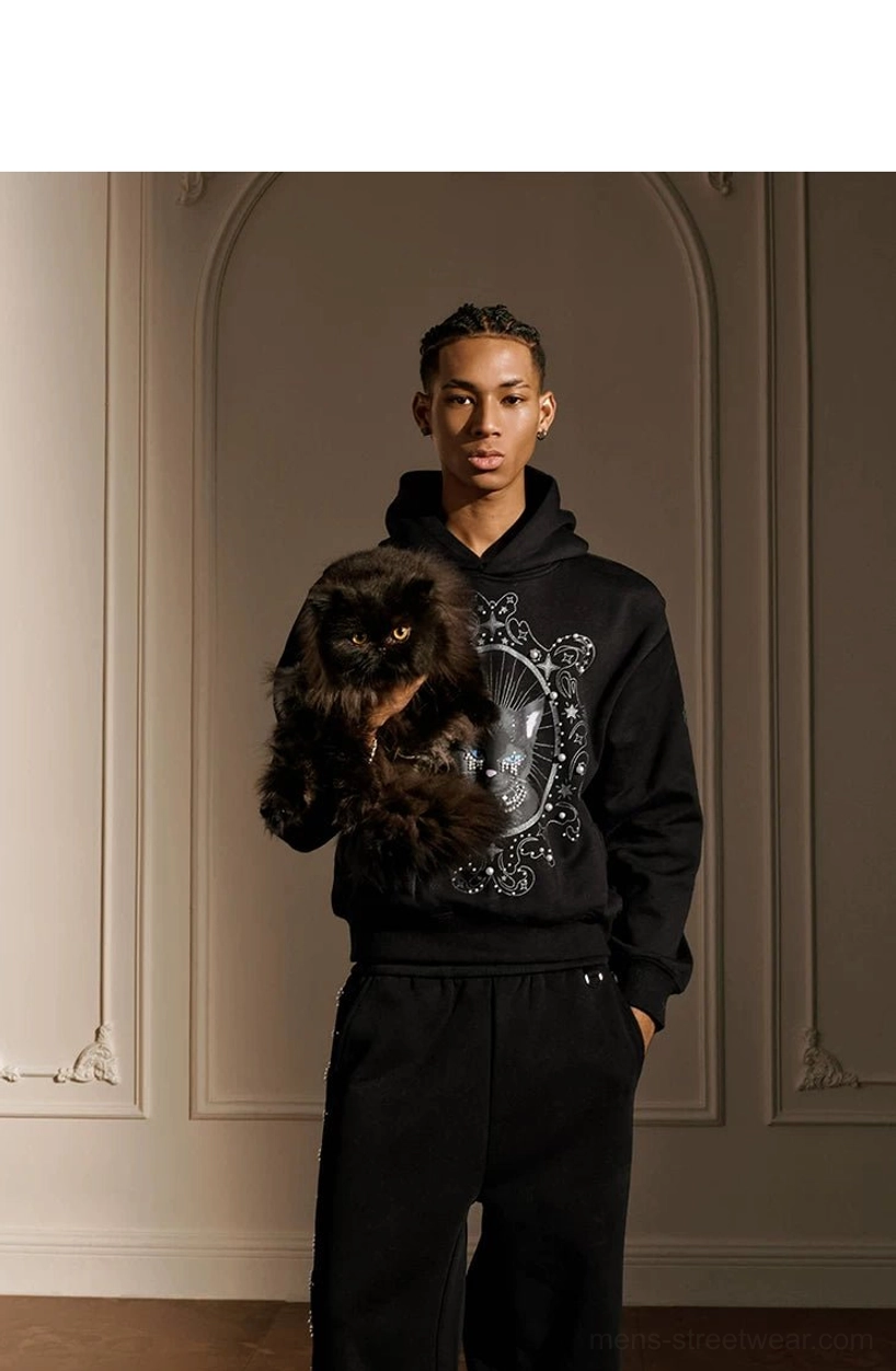 Male model holding black cat while wearing pearl embellished mystic cat gothic streetwear hoodie