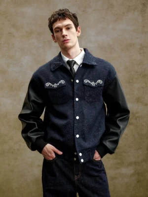 Front view of a pearl embellished navy varsity jacket with black faux leather contrast sleeves, snap buttons, textured body, and ornate chest details
