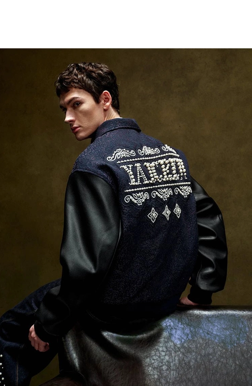 Seated back close-up of a pearl embellished varsity jacket highlighting oversized pearl lettering, ornate back artwork, contrast sleeves, and ribbed hem