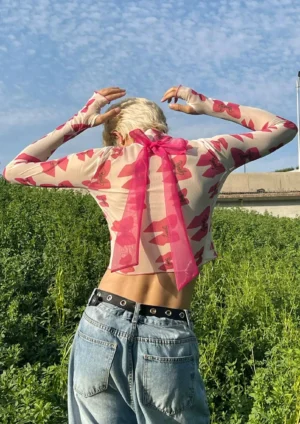 Back view of pink bow print sheer mesh cropped top with oversized detachable back bow sash and long sleeves