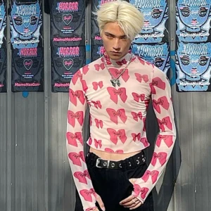 Front view of fitted pink bow print sheer mock neck cropped top styled with belted black streetwear trousers