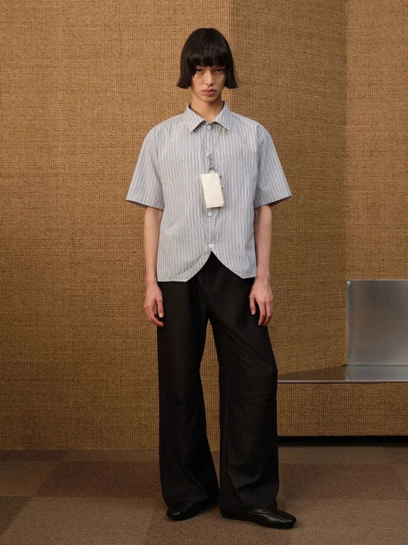 Full body front view of a male model styling a white grey pinstripe curved hem shirt with black wide leg trousers