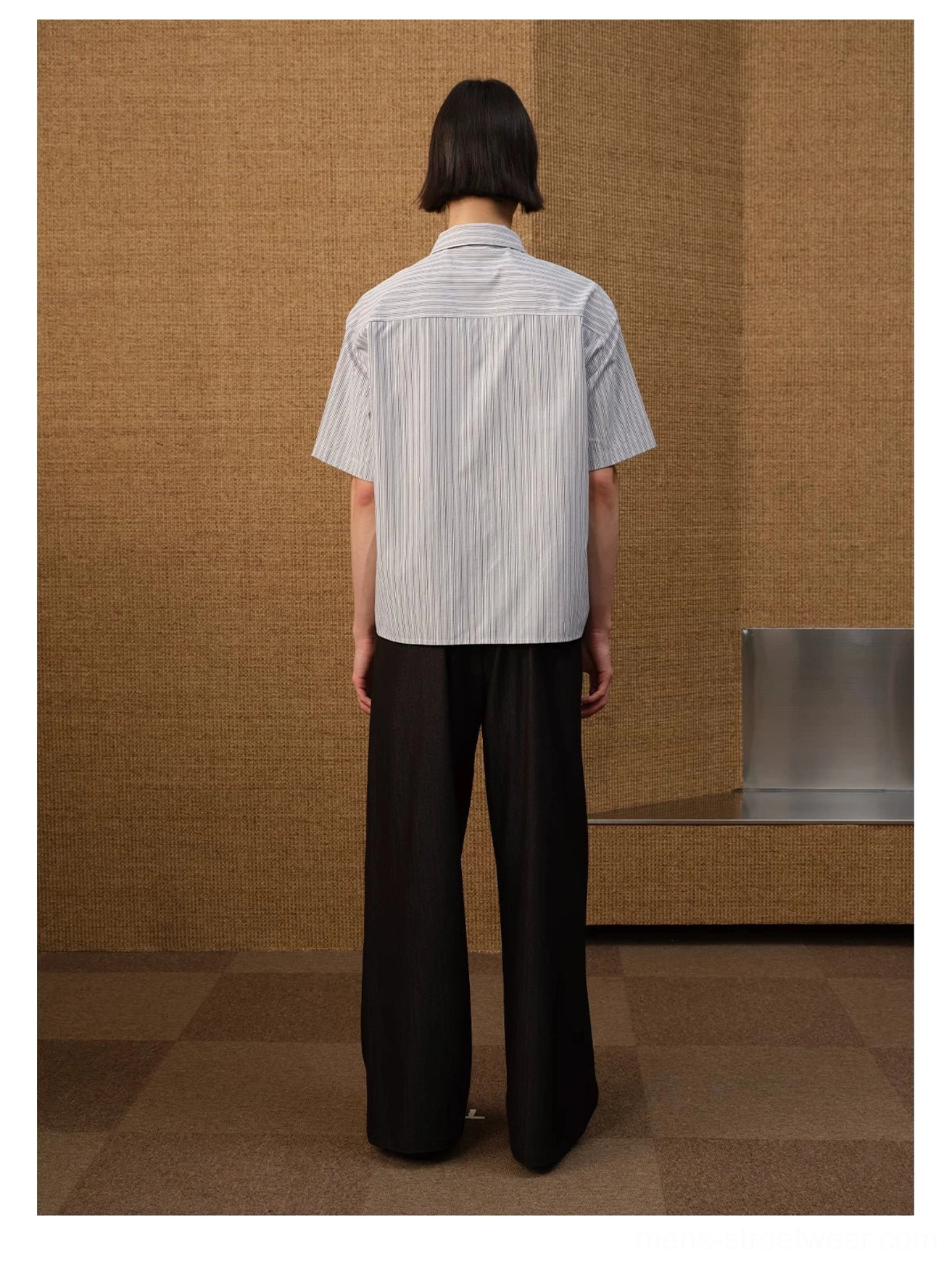 Full body rear view of a model wearing a white grey pinstripe shirt with curved back hem and black wide leg trousers