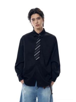 Male model wearing an oversized black Oxford shirt with a striped necktie and wide-leg blue jeans in a minimalist studio