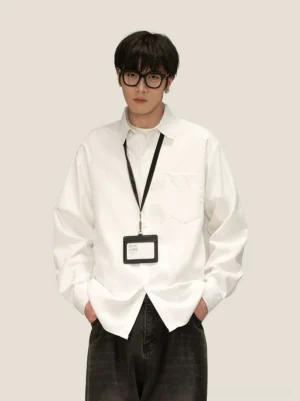 Male model wearing an oversized white Oxford shirt with black frame glasses dark jeans and an ID badge lanyard