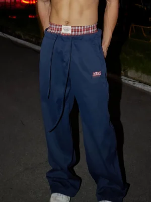 Navy blue plaid waist wide-leg drawstring pants styled on a male model in an outdoor night streetwear setting