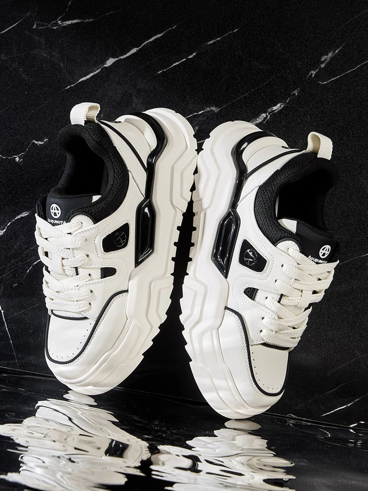 Paired chunky platform sneakers oblique overhead on black marble reflective background showing shoe tongue logo and product reflection
