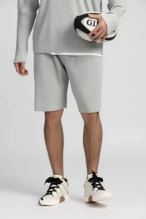 Light gray pleated tech shorts with relaxed straight legs shown from a low angle on a studio gray background