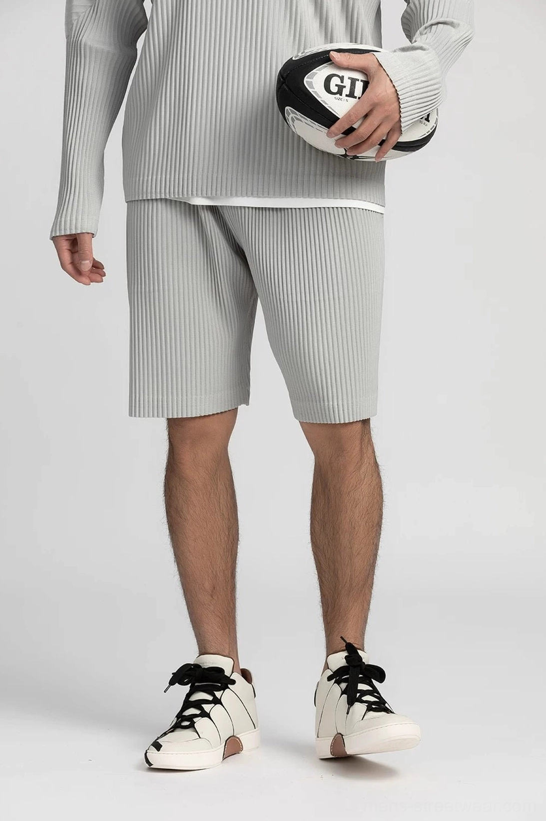 Light gray pleated tech shorts with relaxed straight legs shown from a low angle on a studio gray background