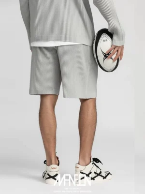 Light gray pleated tech shorts styled with a matching long sleeve top and two tone casual sneakers