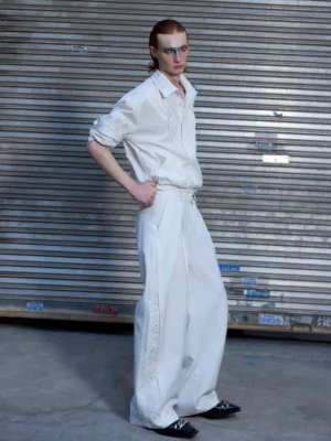 White pleated wide-leg cargo trousers styled with a white shirt and leather loafers in an outdoor streetwear setting