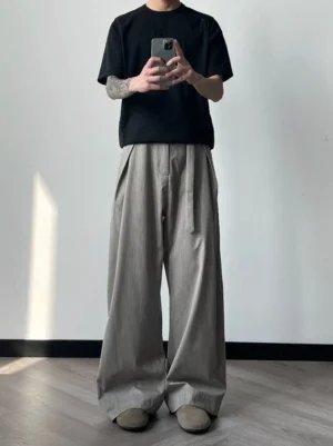 Model wearing relaxed pleated wide-leg tie-waist trousers with black t-shirt and brown leather loafers in a minimalist streetwear outfit
