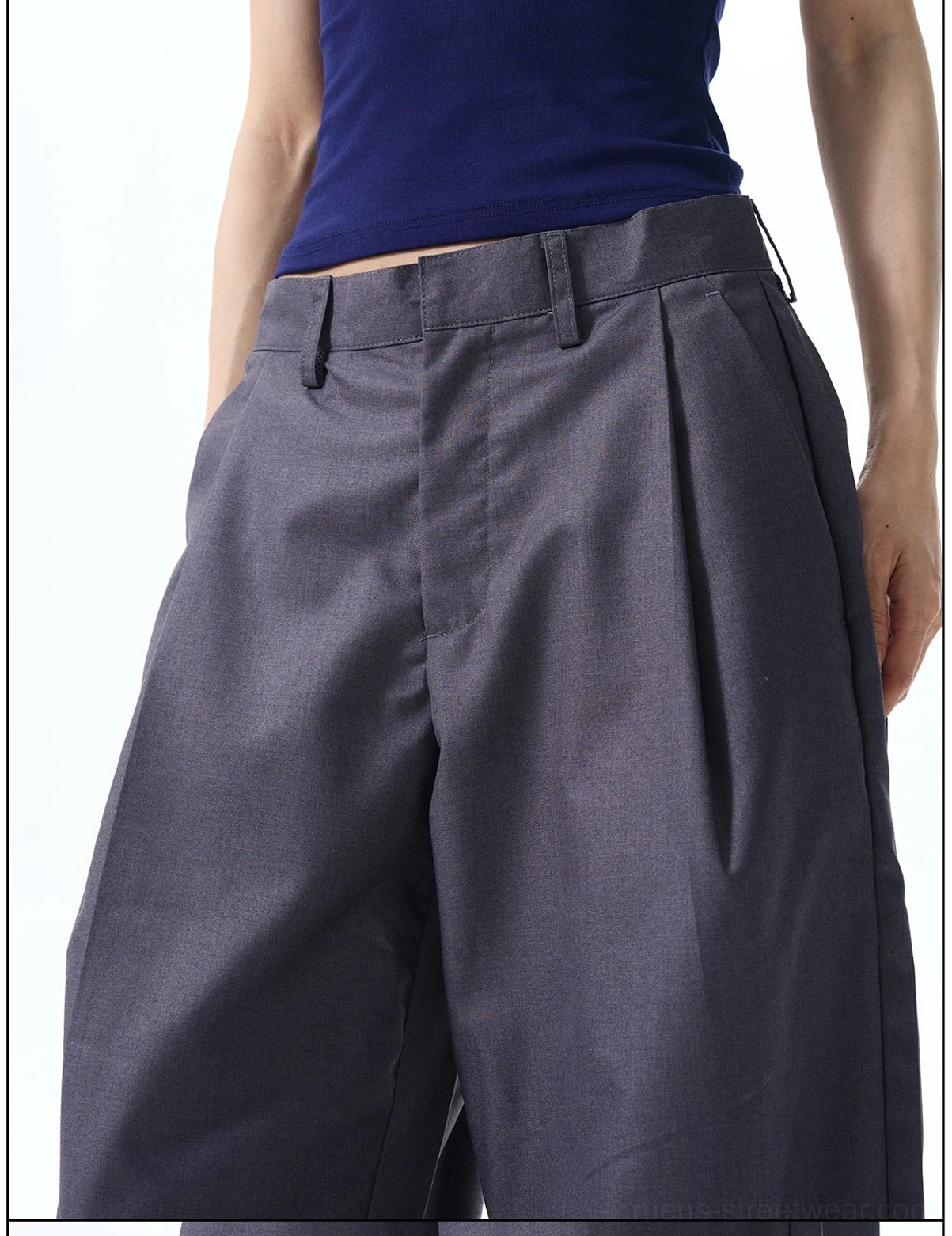 Close-up of slate grey pleated wide leg trousers showing belt loops button fly and smooth suiting texture