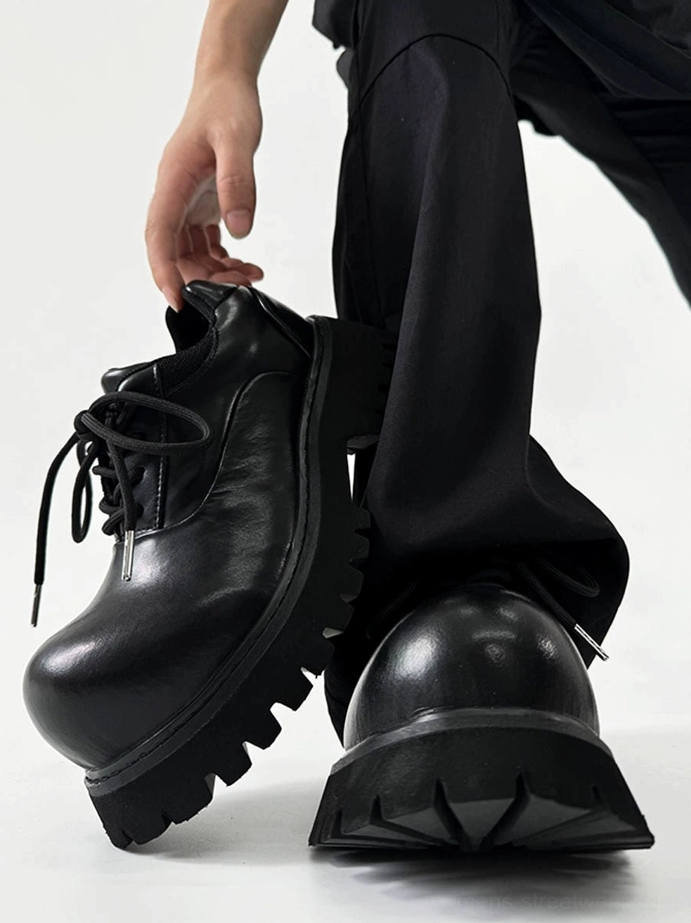 Polished black platform Derby shoes with chunky lug sole shown in a top angled view with black streetwear trousers