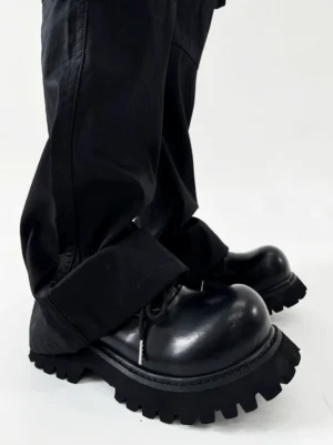 Side profile of polished black lug sole Derby shoes worn with loose black workwear trousers