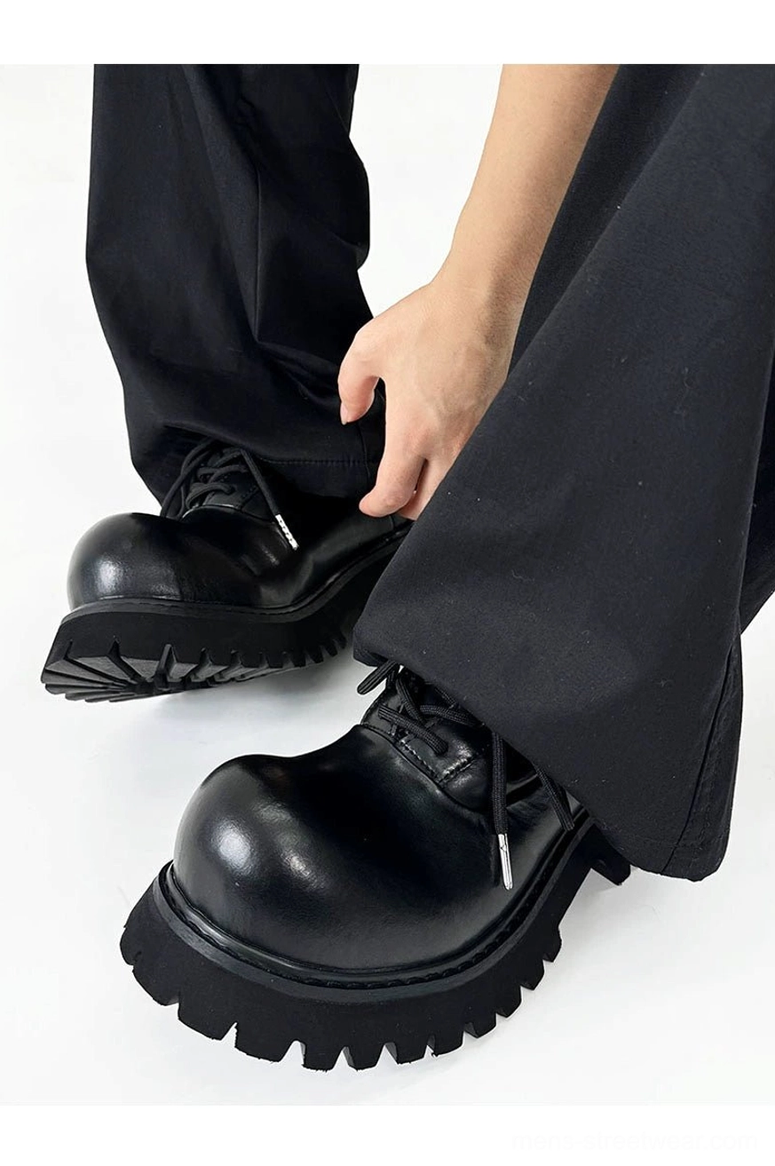 Black platform Derby shoes with glossy upper and rugged tread sole worn in a monochrome streetwear outfit