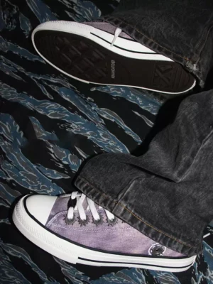 Purple distressed low-top skate sneakers worn with dark washed denim in overhead streetwear styling view