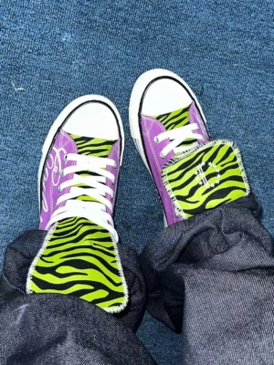 Overhead view of purple zebra tongue canvas sneakers worn with dark denim jeans showing white laces and vulcanized rubber soles