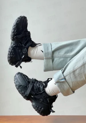 Black chunky racing sneakers worn with light blue jeans and white socks showing lace-up front and tactical strap details