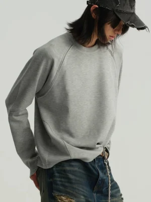 Light heather grey raglan crewneck sweatshirt styled with distressed wide leg jeans and a vintage baseball cap in a modern streetwear outfit