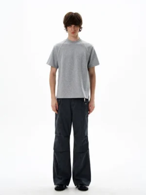 Front view of a heather grey raglan sleeve cropped T-shirt styled with dark wide-leg trousers in a minimalist streetwear studio