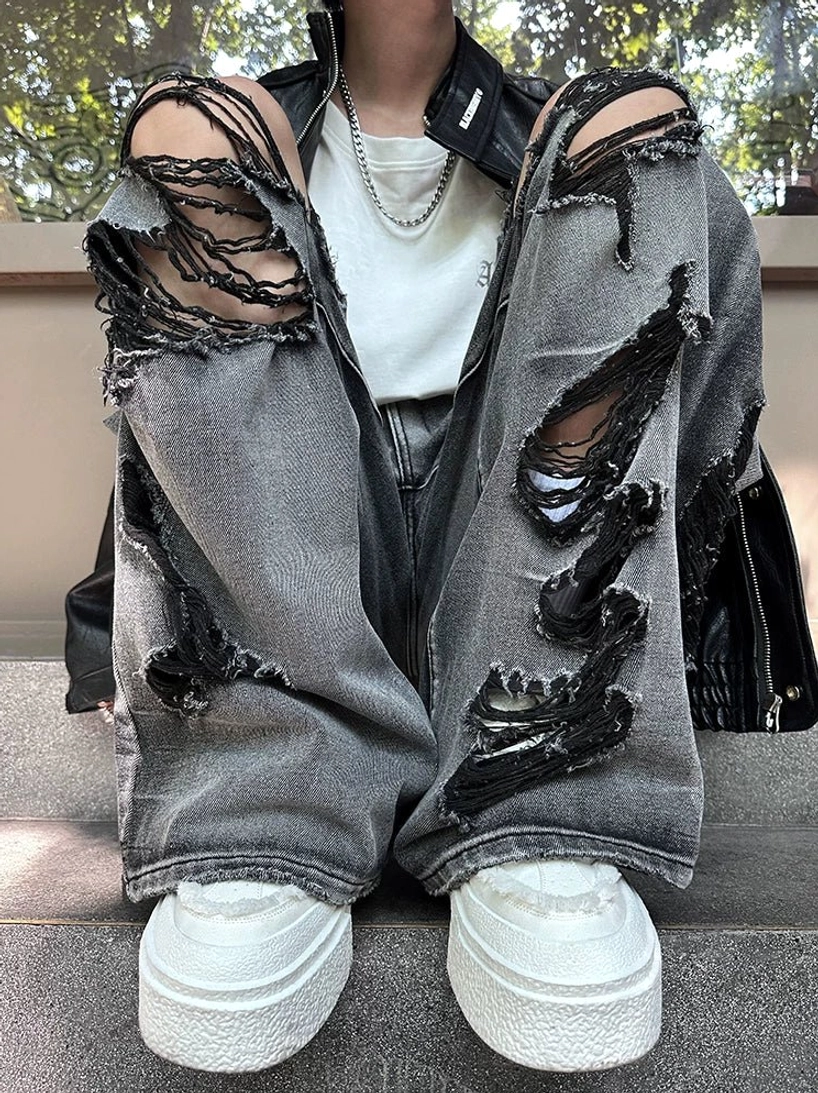 Top-down view of faded black-gray distressed jeans showing oversized destroyed holes, frayed edges, wide legs, and streetwear styling