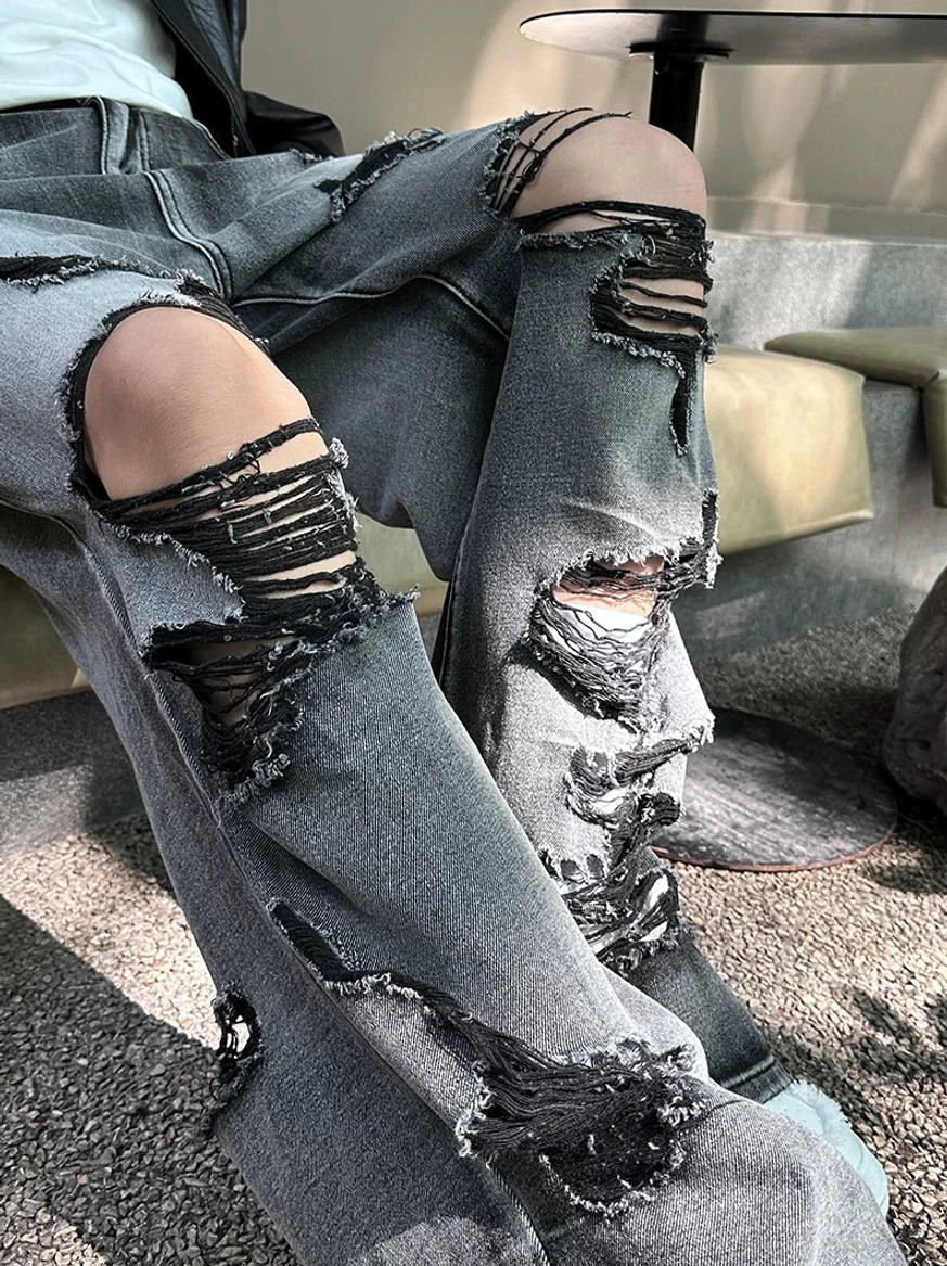 Close-up of heavily distressed gray jeans with frayed knee rips styled with white platform sneakers for a Korean streetwear look